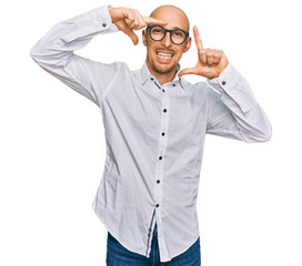 Bald man with beard wearing business shirt and glasses smiling making frame with hands and fingers...