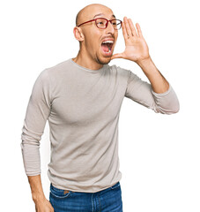 Bald man with beard wearing casual clothes and glasses shouting and screaming loud to side with hand on mouth. communication concept.