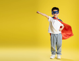 full body image of a boy wearing a superhero shirt posing on a yellow background