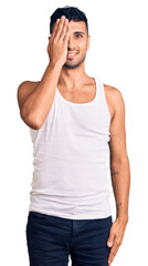 Young hispanic man wearing casual clothes covering one eye with hand, confident smile on face and surprise emotion.