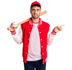 Young hispanic man playing baseball holding bat and ball smiling happy pointing with hand and finger to the side