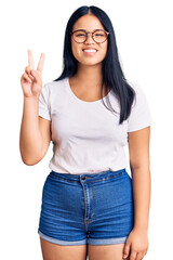 Obraz na płótnie Canvas Young beautiful asian girl wearing casual clothes and glasses showing and pointing up with fingers number two while smiling confident and happy.