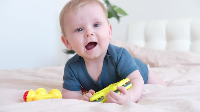 baby boy in blue bodysuit plays with colorful plastic rattle on bed