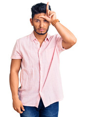 Fototapeta premium Handsome latin american young man wearing casual summer shirt making fun of people with fingers on forehead doing loser gesture mocking and insulting.