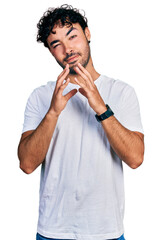 Hispanic young man with beard wearing casual white t shirt hands together and fingers crossed smiling relaxed and cheerful. success and optimistic