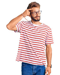 Fototapeta premium Handsome blond man with beard wearing casual clothes and glasses pointing unhappy to pimple on forehead, ugly infection of blackhead. acne and skin problem