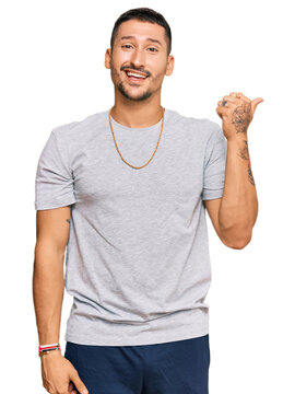 Handsome man with tattoos wearing 90s style smiling with happy face looking and pointing to the side with thumb up.