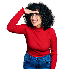 Young middle east girl wearing casual clothes and glasses very happy and smiling looking far away with hand over head. searching concept.