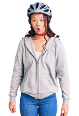Young beautiful chinese girl wearing bike helmet scared and amazed with open mouth for surprise, disbelief face