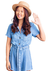 Obraz na płótnie Canvas Young beautiful chinese girl wearing summer hat waiving saying hello happy and smiling, friendly welcome gesture