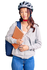 Young beautiful chinese girl wearing student backpack and bike helmet holding book thinking attitude and sober expression looking self confident