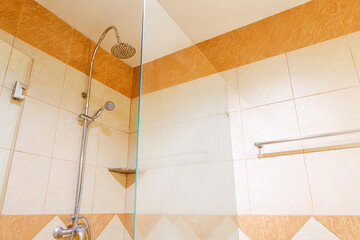 Stainless steel hanging shower on tile wall with glass shower Enclosures inside of modern bathroom,...