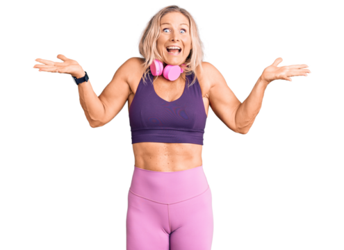Middle age fit blonde woman wearing gym clothes and using headphones celebrating crazy and amazed for success with arms raised and open eyes screaming excited. winner concept