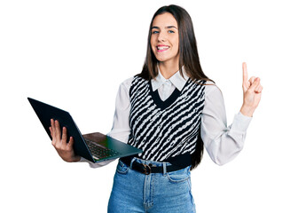 Young brunette teenager working using computer laptop smiling with an idea or question pointing finger with happy face, number one