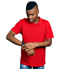 Young african american man wearing casual red t shirt checking the time on wrist watch, relaxed and confident
