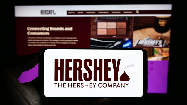 Stuttgart, Germany - 07-02-2023: Person holding smartphone with logo of US food business The Hershey Company on screen in front of website. Focus on phone display.