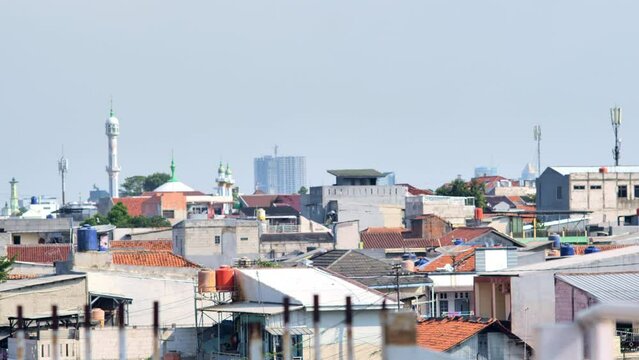 A view of Jakarta's lower middle class neighborhoods. Shot on a hot afternoon with a telephoto lens and panning motion. Depicts urban population density and disorder.