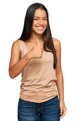 Beautiful hispanic woman wearing casual clothes doing happy thumbs up gesture with hand. approving expression looking at the camera showing success.