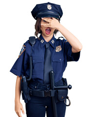 Young beautiful girl wearing police uniform peeking in shock covering face and eyes with hand, looking through fingers with embarrassed expression.