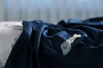 Unrolled condom on bed in bedroom. Safe sex
