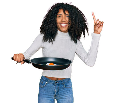 Young african american girl holding skillet with fried egg surprised with an idea or question pointing finger with happy face, number one
