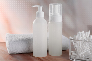 Obraz na płótnie Canvas Bottles with face cleansing products, cotton buds and towel on beige marble table