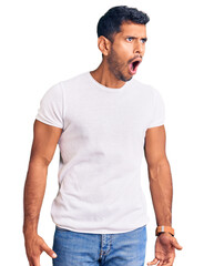 Young latin man wearing casual clothes angry and mad screaming frustrated and furious, shouting with anger. rage and aggressive concept.