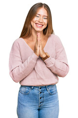 Beautiful blonde woman wearing casual winter pink sweater praying with hands together asking for forgiveness smiling confident.