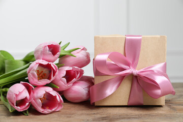 Beautiful gift box with bow and pink tulips on wooden table, closeup