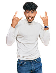 Young arab man wearing casual winter sweater shouting with crazy expression doing rock symbol with hands up. music star. heavy music concept.