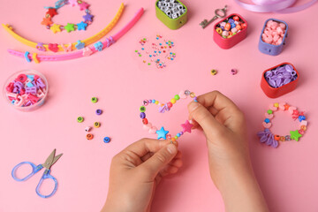 Child making beaded jewelry and different supplies on pink background, above view. Handmade...