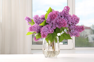 Beautiful lilac flowers in vase on white wooden table indoors
