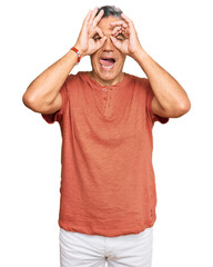 Fototapeta premium Handsome middle age man wearing casual clothes doing ok gesture like binoculars sticking tongue out, eyes looking through fingers. crazy expression.