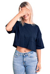 Young beautiful blonde woman wearing casual t-shirt smiling and laughing with hand on face covering eyes for surprise. blind concept.