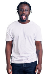 Fototapeta premium Young african american man with braids wearing casual white tshirt sticking tongue out happy with funny expression. emotion concept.