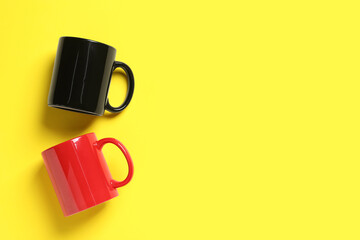 Black and red ceramic mugs on yellow background, flat lay. Space for text