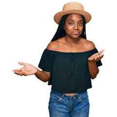 Young african american woman wearing summer hat clueless and confused expression with arms and...