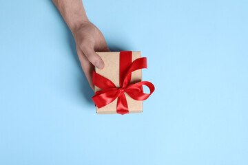Man holding gift box with red bow on light blue background, top view