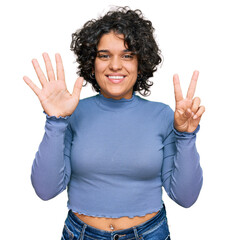 Young hispanic woman with curly hair wearing casual clothes showing and pointing up with fingers number seven while smiling confident and happy.