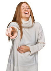 Young irish woman wearing casual winter sweater laughing at you, pointing finger to the camera with...