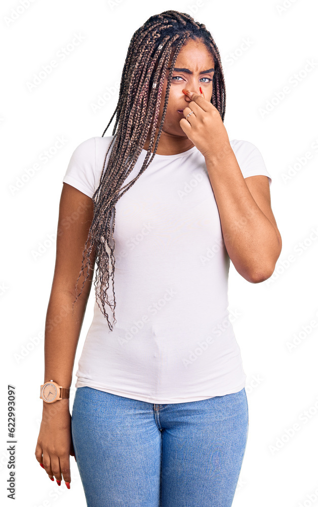 Sticker Young african american woman with braids wearing casual clothes smelling something stinky and disgusting, intolerable smell, holding breath with fingers on nose. bad smell