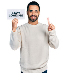 Young hispanic man with beard holding lazy loading banner smiling with an idea or question pointing finger with happy face, number one