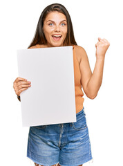Fototapeta premium Young caucasian woman holding blank empty banner screaming proud, celebrating victory and success very excited with raised arms