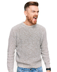 Young redhead man wearing casual winter sweater angry and mad screaming frustrated and furious, shouting with anger. rage and aggressive concept.