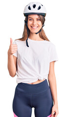 Young beautiful girl wearing bike helmet smiling happy and positive, thumb up doing excellent and approval sign