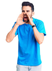 Young handsome man with beard wearing casual t-shirt shouting angry out loud with hands over mouth
