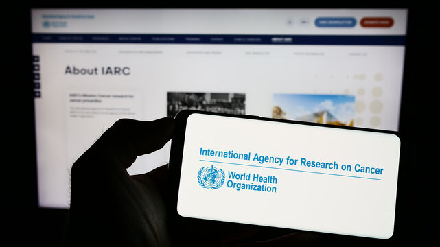 Stuttgart, Germany - 07-04-2023: Person holding cellphone with logo of International Agency for Research on Cancer (IARC) on screen in front of webpage. Focus on phone display.