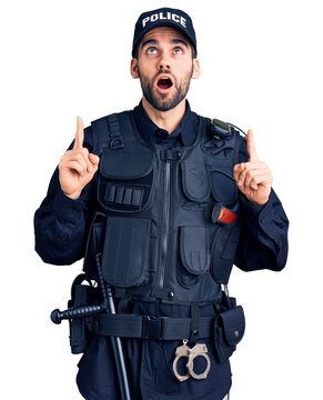 Young handsome man with beard wearing police uniform amazed and surprised looking up and pointing with fingers and raised arms.