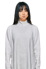 Young brunette woman with bangs wearing casual turtleneck sweater puffing cheeks with funny face....