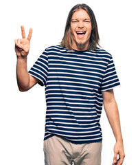 Obraz premium Handsome caucasian man with long hair wearing casual striped t-shirt smiling with happy face winking at the camera doing victory sign. number two.